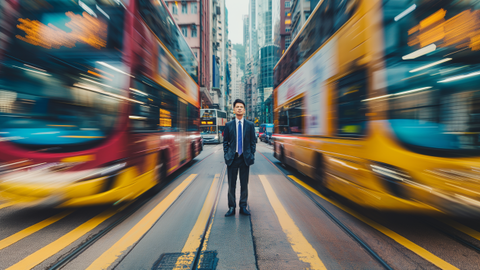 Porträt einer Geschäftsperson, die in der Mitte der Straße steht, während Autos und Busse mit extremer Bewegungsunschärfe vorbeifahren. Die Busse und die Linien auf der Straße sind mehrheitlich gelb. | © wob AG