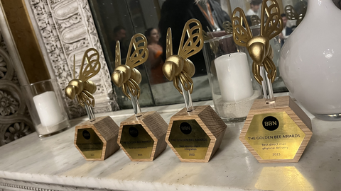 Zu sehen ist ein Foto von vier Awardtrophäen in Form von goldenen Biene. Die Goldenen Bienen stehen auf einem Sideboard. Auf den Plaketten der Trophäen ist das Logo von BBN zu sehen sowie die Bezeichnung „Golden Bee Awards“.