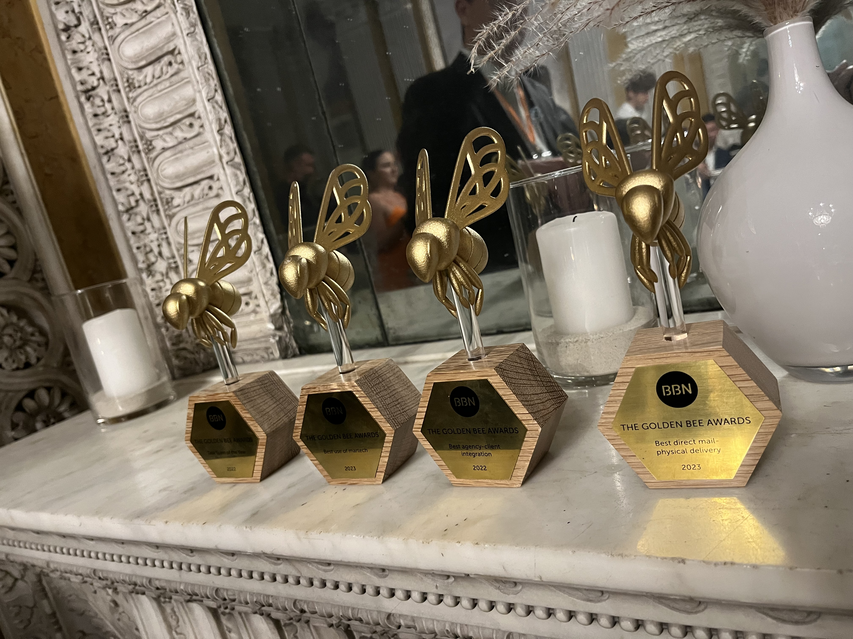 Zu sehen ist ein Foto von vier Awardtrophäen in Form von goldenen Biene. Die Goldenen Bienen stehen auf einem Sideboard. Auf den Plaketten der Trophäen ist das Logo von BBN zu sehen sowie die Bezeichnung „Golden Bee Awards“.